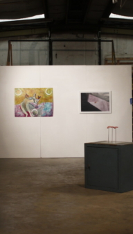 image of a warehouse gallery, a long white wall stands in a dim, high-ceiling room