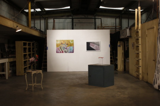image of a warehouse gallery, a long white wall stands in a dim, high-ceiling room