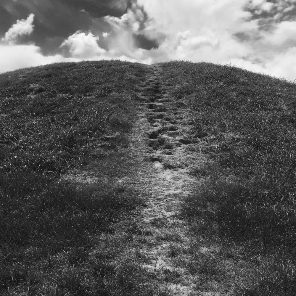 a black and white image of a large earthen mound with a path of footprints running down the middle.