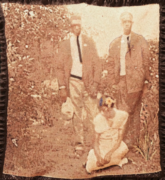 in a sepia colored screenprint, two Black men stand next to each other outdoors, a woman sits between them