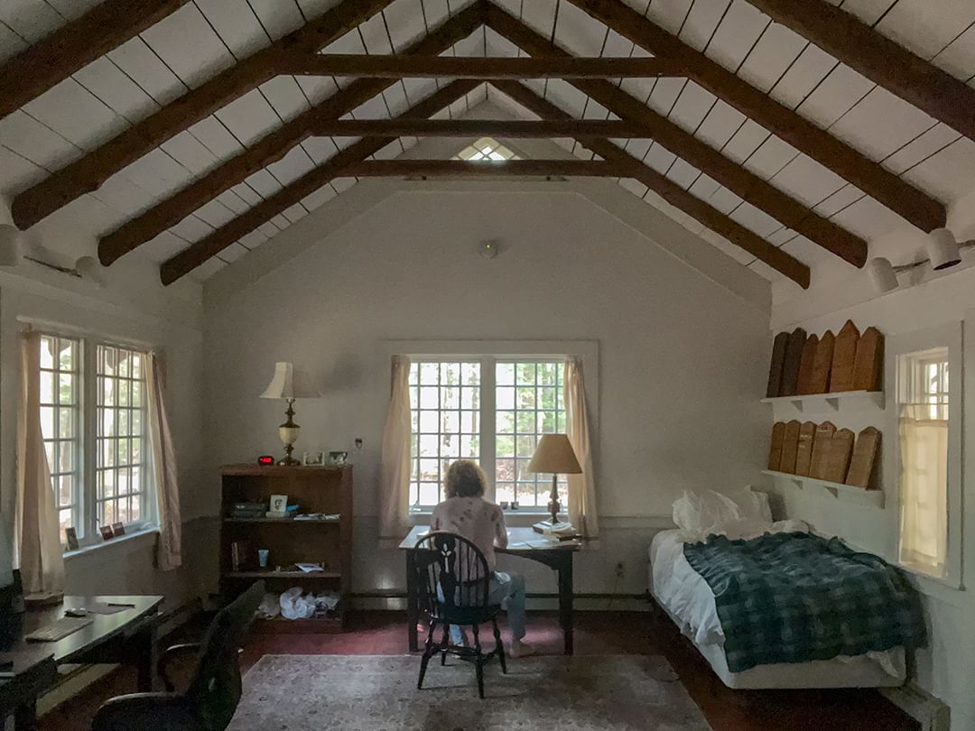 Horizontal image of room with assorted furniture and person with back to camera, sitting and working at desk