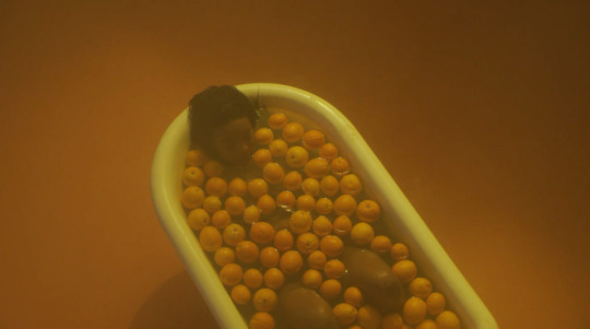 orange tinted image of woman in bathtub surrounded by oranges