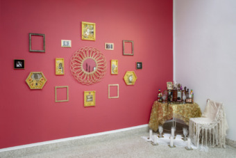 installation view of pink wall with adorned works and a floor altar