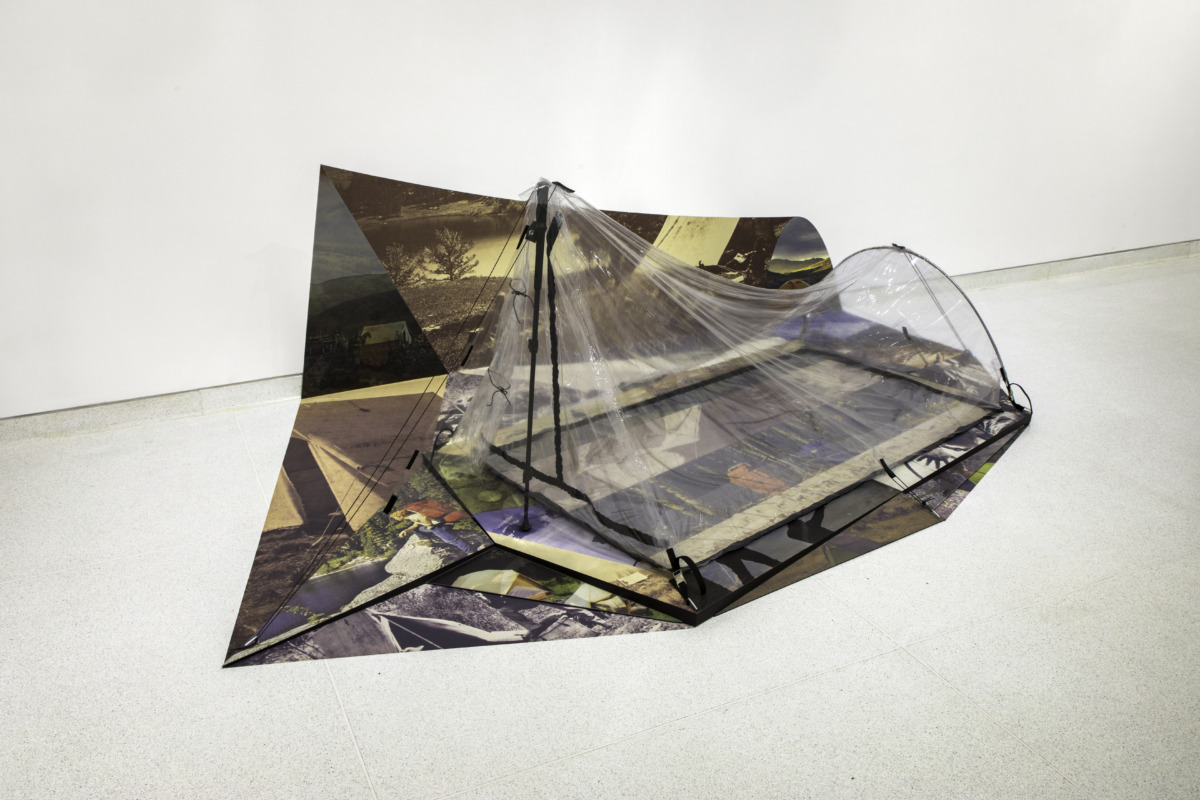 A clear plastic two-person tent on top of large scale images that mimic a shadow on the ground and wall. 