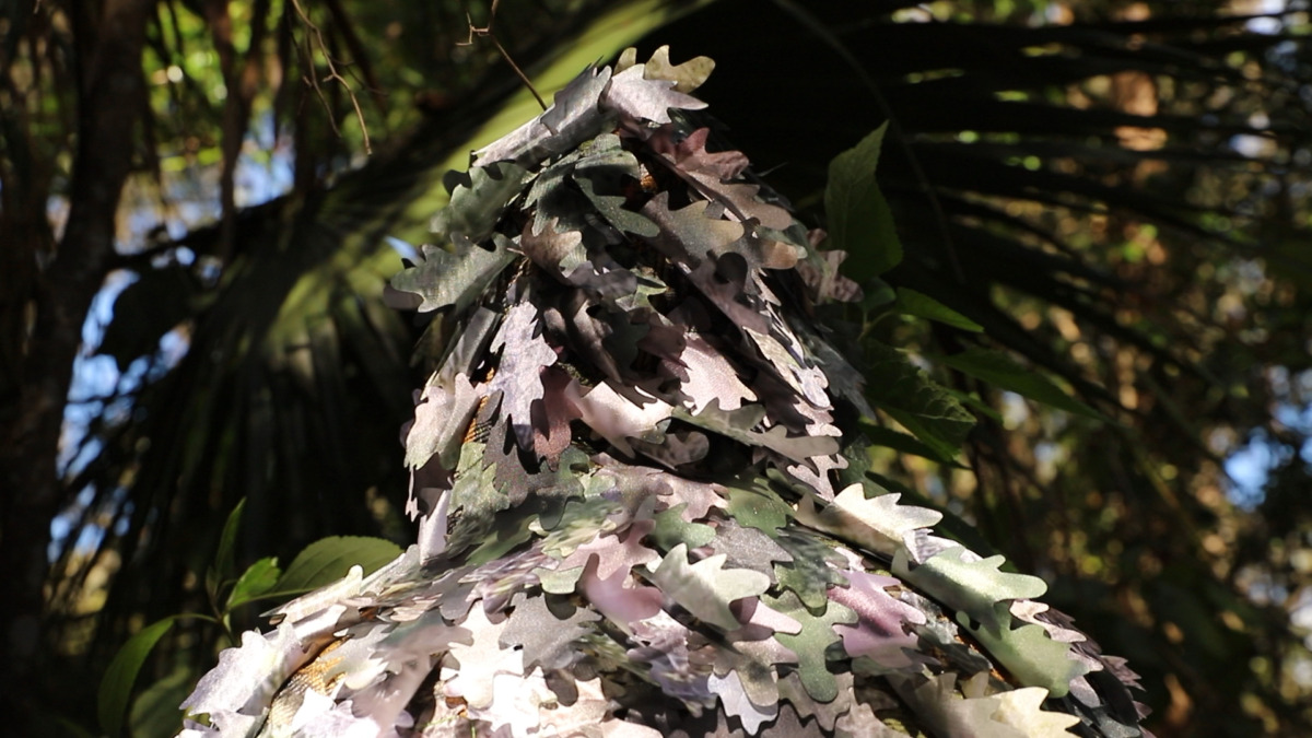 figure facing away from the camera that is covered in artificial leaves