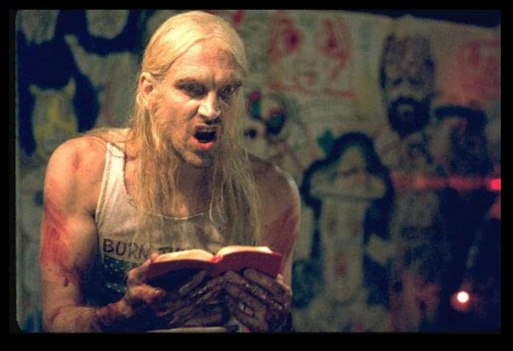 An angry blood covered man reading from a small red book