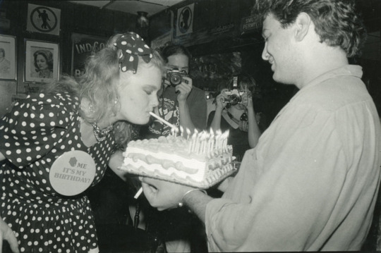 black and white photograph of woman lighting cigarette with candle from birthday cake while man holds cake