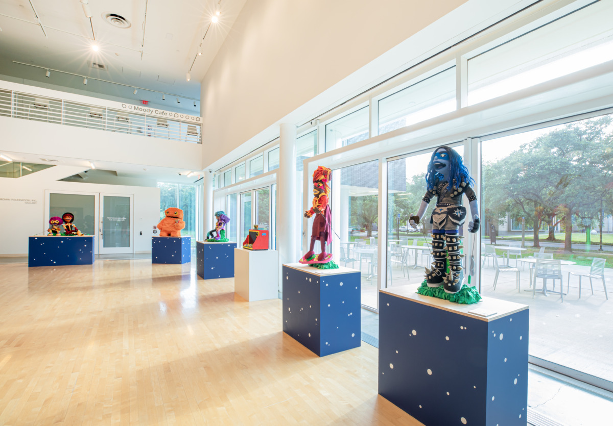 Brightly colored characters on pedestals facing the away from large windows. 