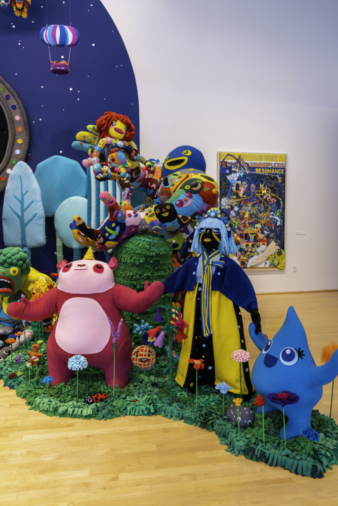 Closeup of characters standing together in artificial grass and in front of a curved, starry sky. 