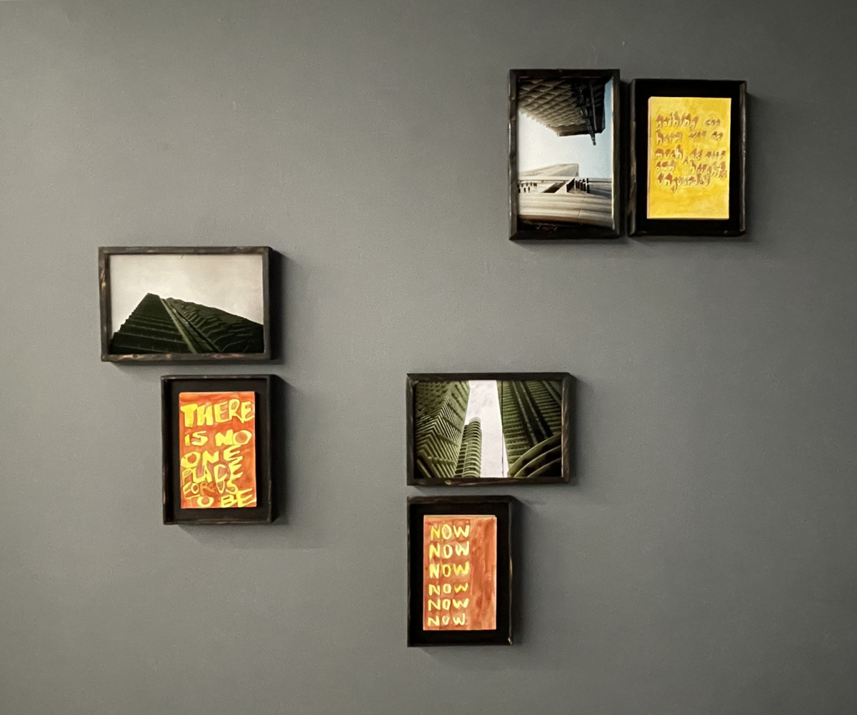 gray wall with six framed works of art three are red and yellow three are photos of high rise condo buildings.