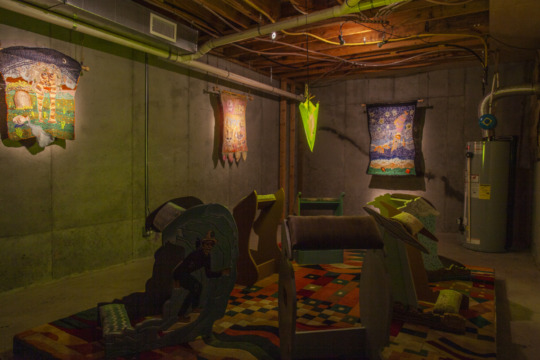 installation view of dimly lit exhibition with sculptures and wall hangings