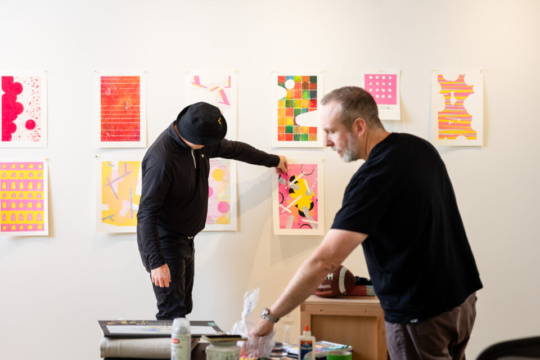 two white men work together in placing artwork on a wall